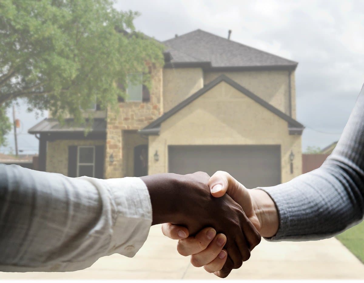 Firm handshake in front of a two-story home; leafy tree in the upper left corner.