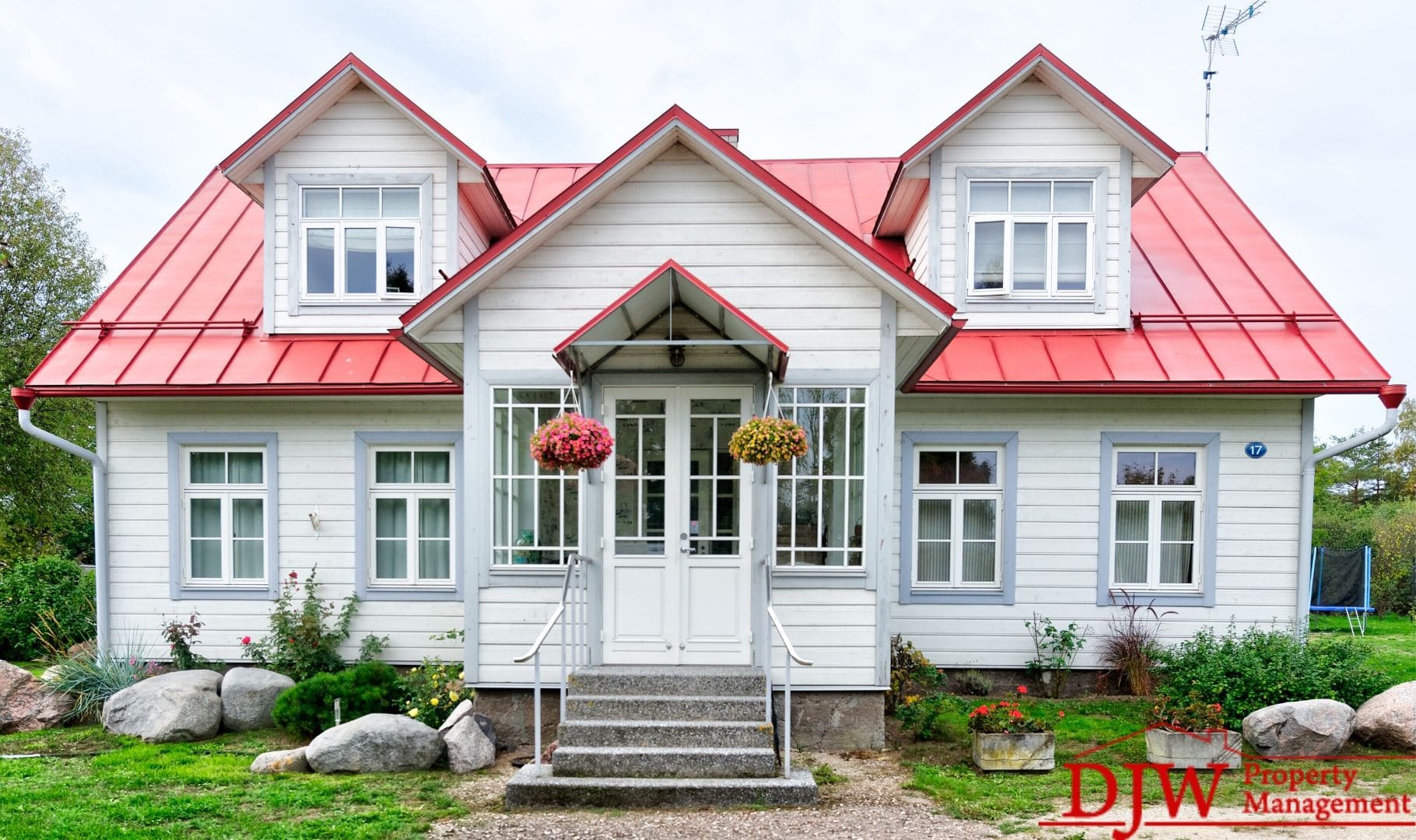 A cute little house; white siding with a red roof and lots of windows. Hanging flower baskets show that it is springtime.