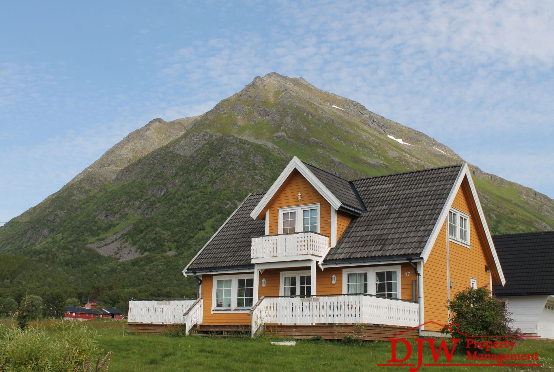 A yellow two-story home with white accents in front of a hill.