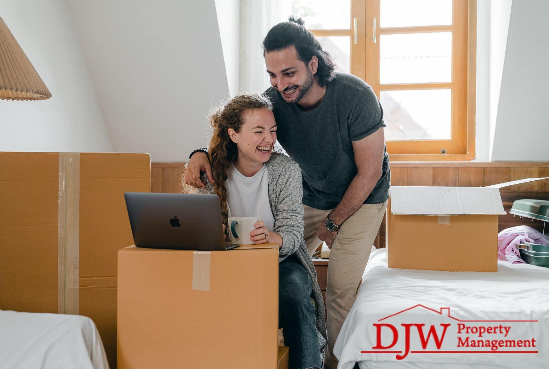 A happy couple looks at a laptop propped up on moving boxes.