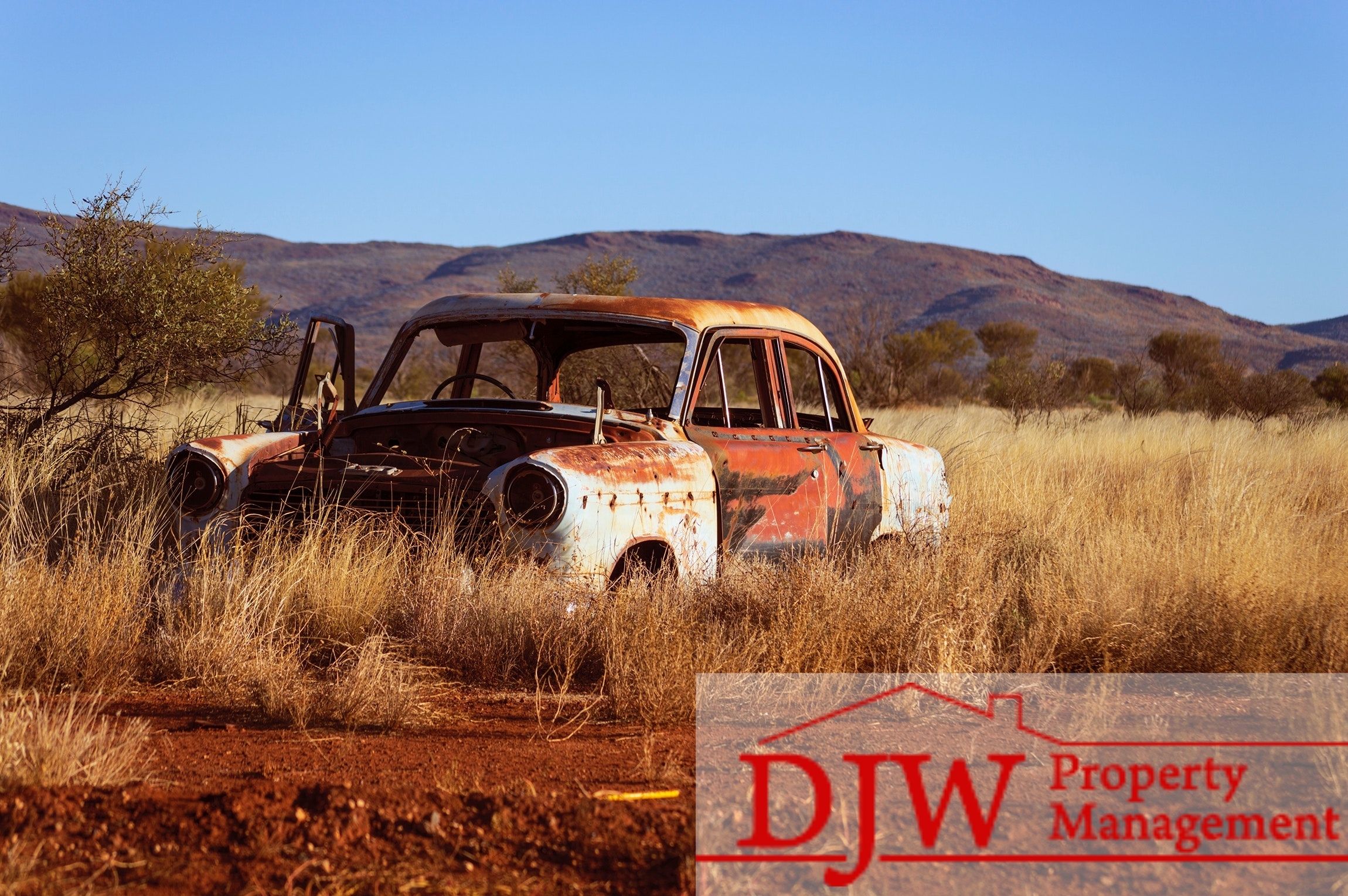 Rusted abandoned car in the grass with hills in the background