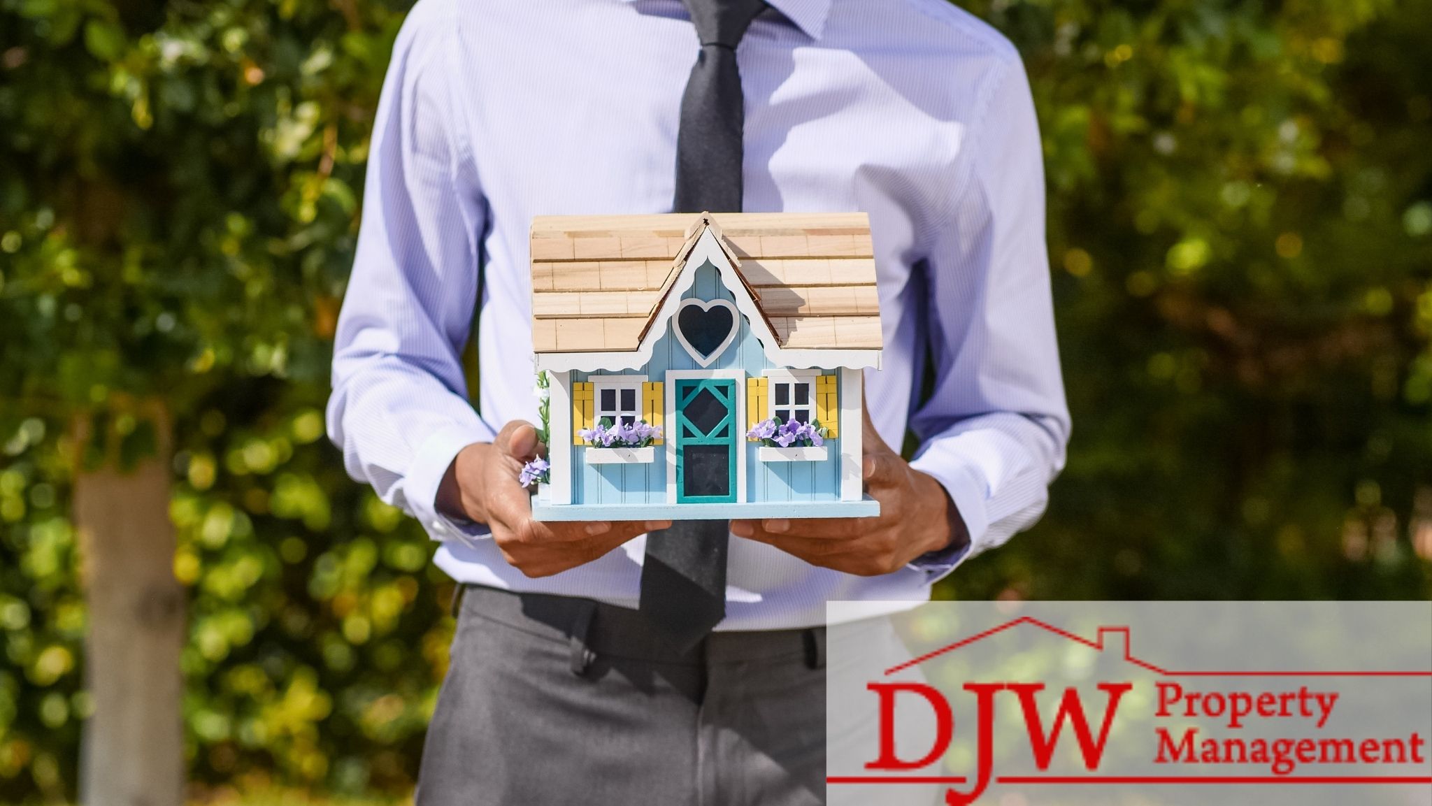 A realtor in a purple shirt holding a small house with a heart-shaped window.