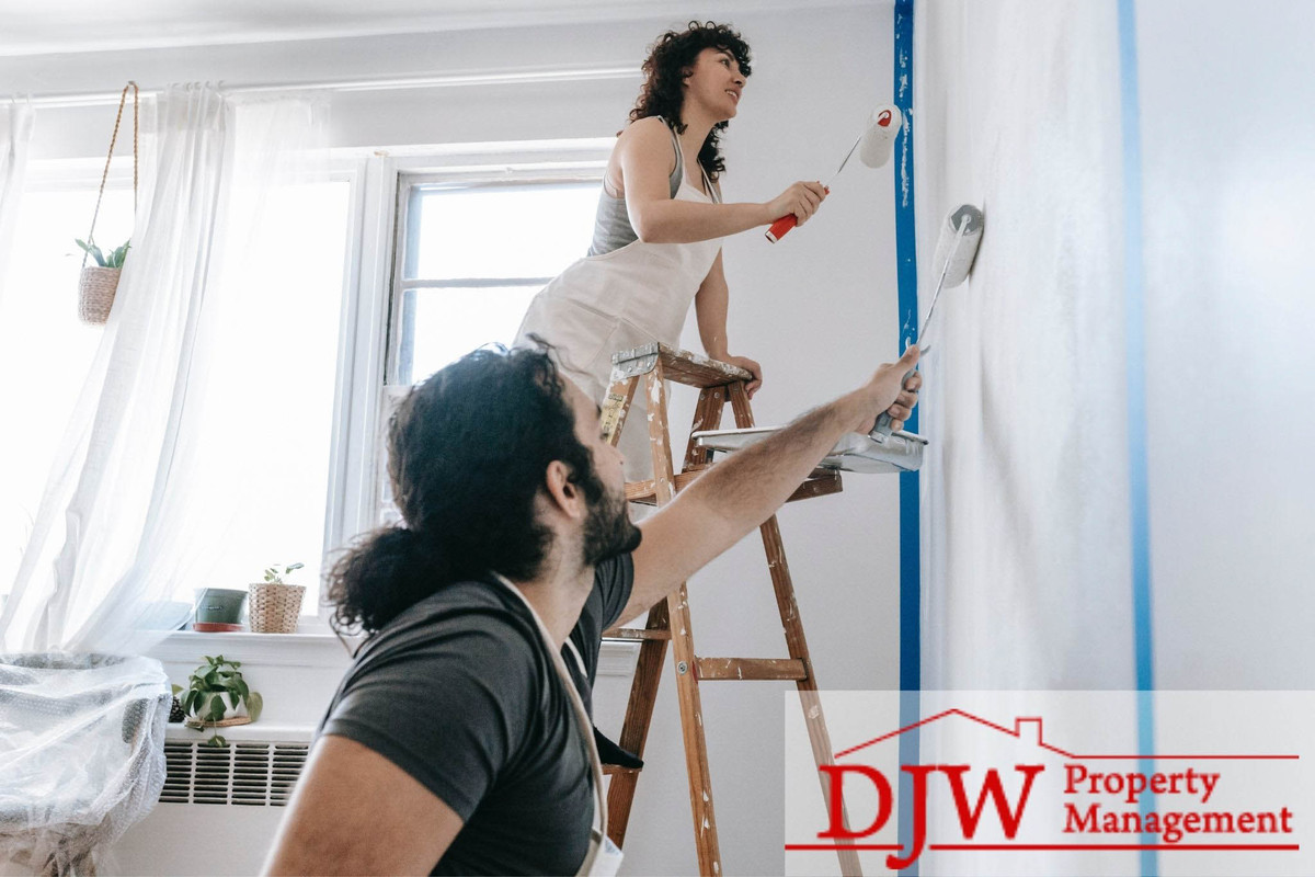 A couple painting a wall in a white room.