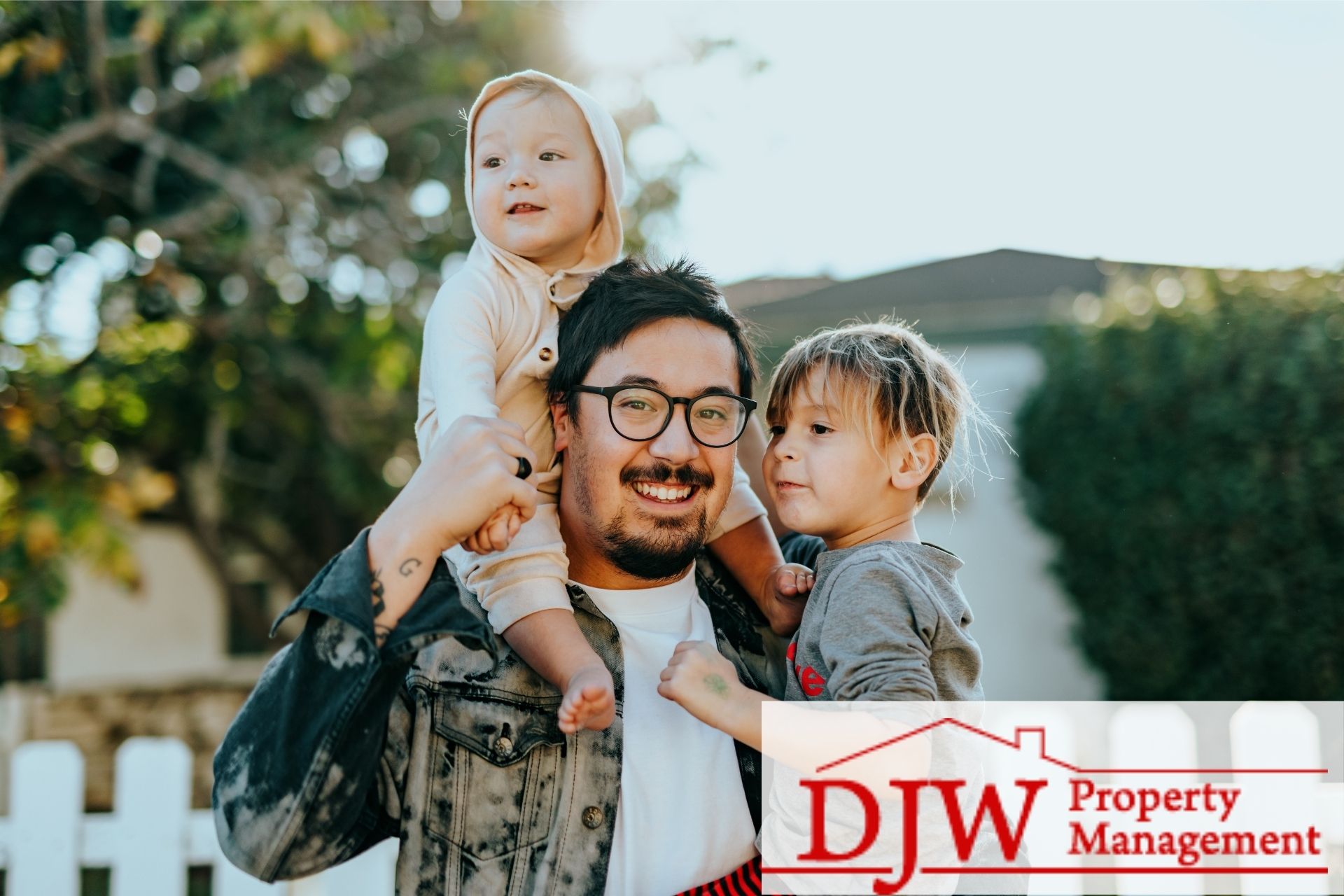 A dad and his two kids smiling in front of a white picket fence and house.